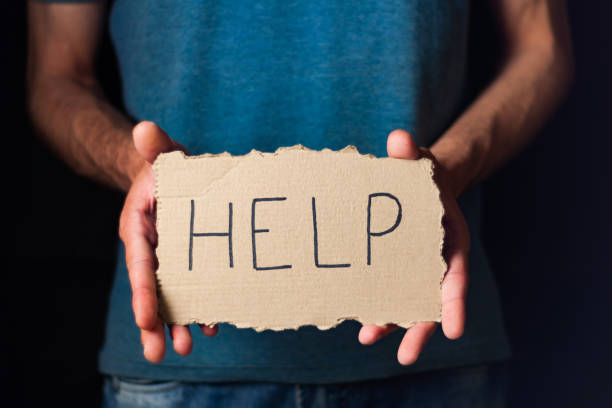 istock Man showing worn rectangle cardboard with handwritten inscription help on black background 974779718
