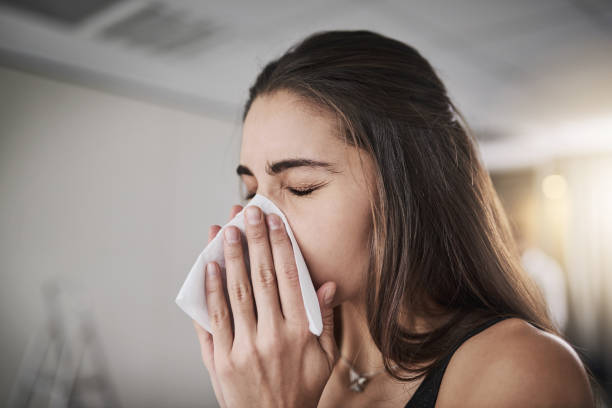 Flu season's coming knocking Shot of a young woman blowing her nose cold virus stock pictures, royalty-free photos & images