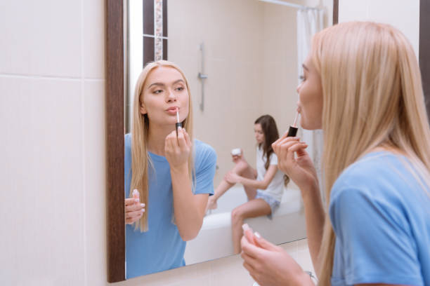 istock attractive girl applying lips gloss in bathroom 974788744