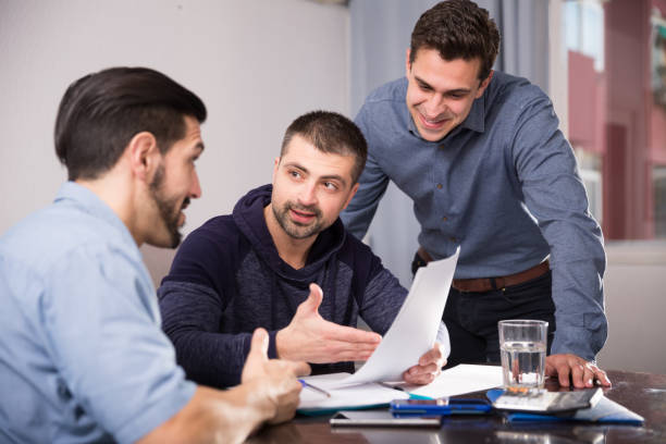 istock Two positive men helping friend with documents at table 974789278