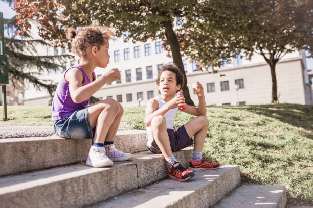 istock Cute mixed race siblings playing outdoors in public park, blowing soap bubbles 974793130