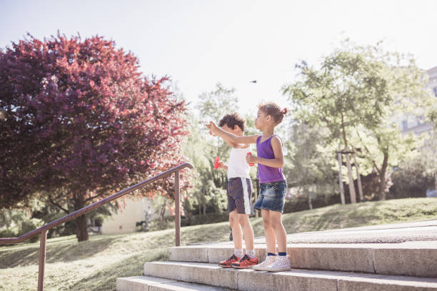 istock Cute mixed race siblings playing outdoors in public park, blowing soap bubbles 974793318