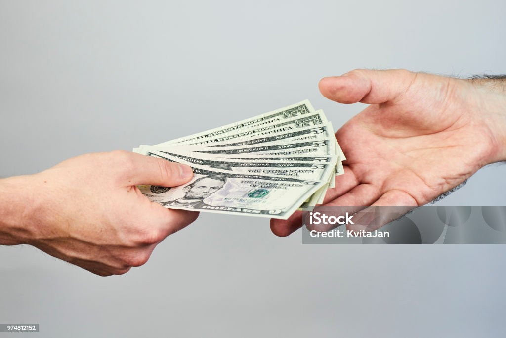 Business closeup of two hands exchanging dollars on grey background. Currency Stock Photo