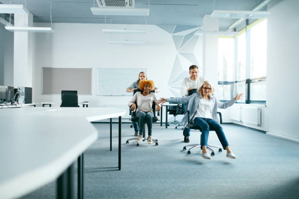 Office. People Having Fun And Racing On Chairs. Office. People Having Fun And Racing On Chairs. Happy Smiling Young Men And Women In Casual Clothes Having Race At Speed In Modern Light Office. Team Building Event. High Resolution. race office stock pictures, royalty-free photos & images