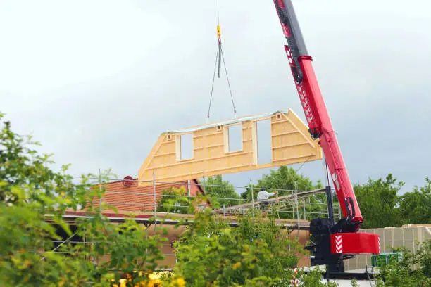 assembly of a prefabricated timber house, crane lifting a gable component in the air