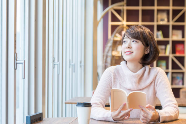 una mujer leyendo un libro en un café - book young adult women student fotografías e imágenes de stock