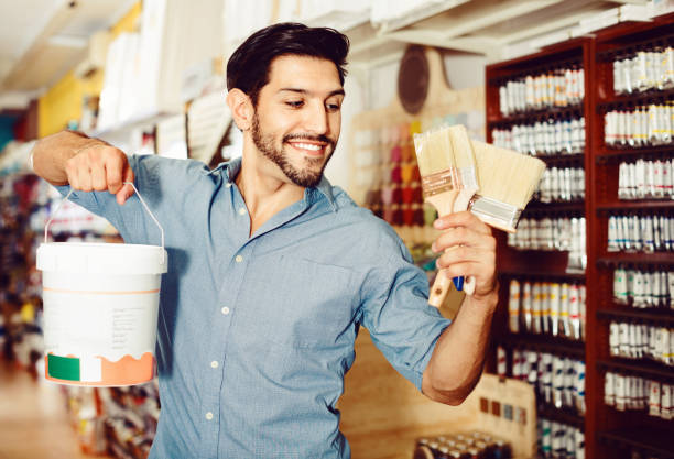 istock Man standing amongst racks in paint store with brushes and paint 974849058
