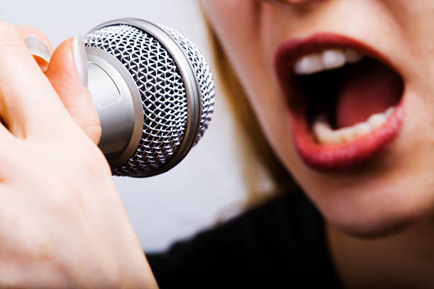 Female singer with disco mic on bokeh light background. Close-up of women's lips painted with burgundy lipstick and retro microphone. Redhead girl starting concert. Copy space for gig posters.