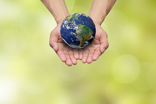Two hands holding the earth in palm gesture on blurred blue map color gradient background.Elements of this image furnished by NASA