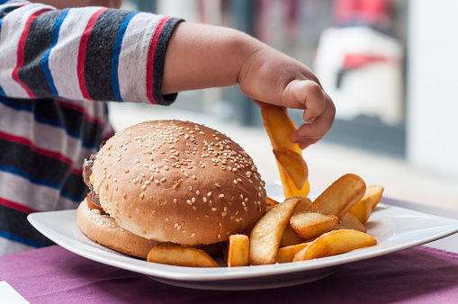 manito de niño comiendo hamburguesa y papas fritas en el restaurante photo