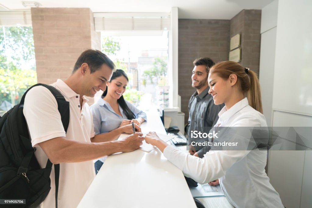 Couple on a romantic getaway doing the check-in at the hotel Happy couple on a romantic getaway doing the check-in at the hotel and talking to the hostess Hotel Stock Photo