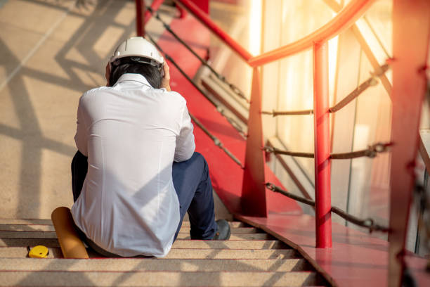 istock Engineer or Architect feeling stressed, worried and tired with his job while sitting on stair with protective safety helmet at construction site.  Problem and failure with construction project concept 974937134