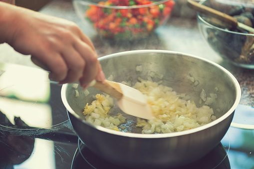 Young woman cooking at home, preparing Spanish seafood paella with shrimp, mussels, octopus, and vegetables.