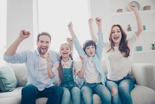 Positive cheerful crazy triumphants laughing family with two kids keeping hands up celebrating event yelling having pleasure enjoyment delight daydream wearing jeans casual outfit