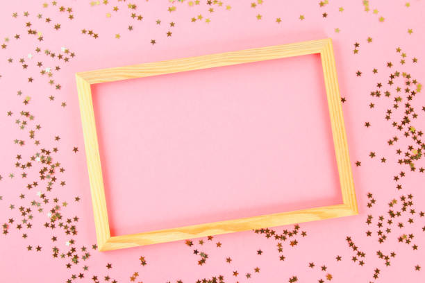 istock A wooden empty frame on a pastel background surrounded by shiny decorative stars and balls. 975025876