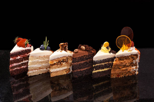 Assorted large pieces of different cakes: chocolate, raspberries, strawberries, nuts, blueberries. Pieces of cakes on a black table