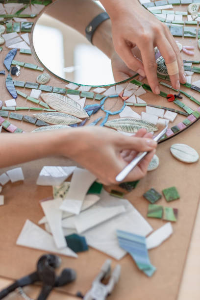 local de trabalho do mestre mosaico: mãos da mulher segurando uma ferramenta para obter detalhes de mosaico no processo de fazer um mosaico - mosaic human hand craft artist - fotografias e filmes do acervo