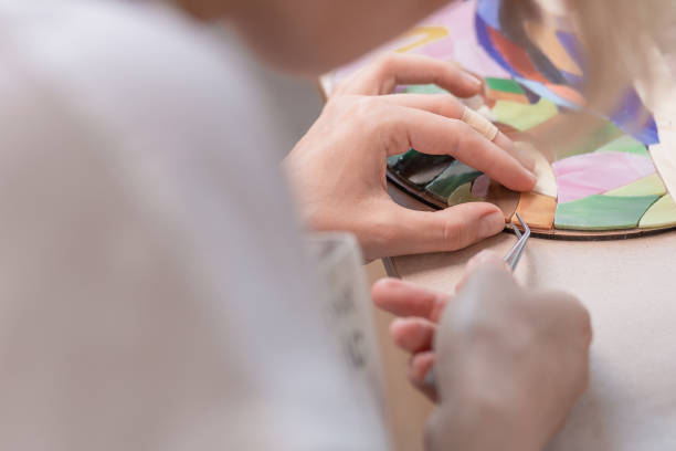 local de trabalho do mestre mosaico: mãos da mulher segurando uma ferramenta para obter detalhes de mosaico no processo de fazer um mosaico - mosaic human hand craft artist - fotografias e filmes do acervo