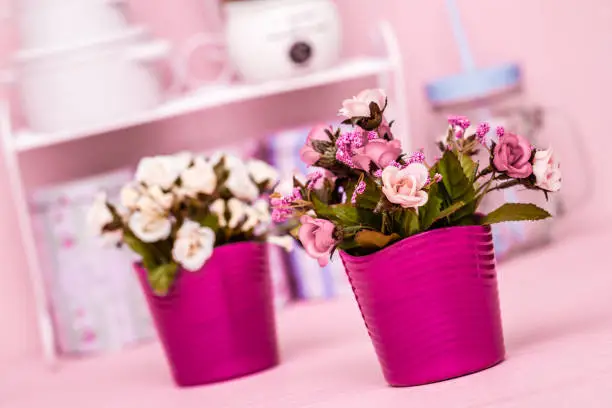 Artificial pink flowers in pink flowerpot on pink wooden background