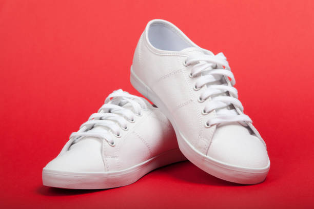 istock Pair of new white sneakers on red background 975104368