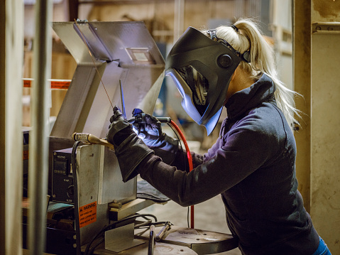 A woman tig welder works in a production facility to repair a piece of equipment.