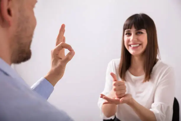 Smiling Young Woman And Man Talking With Sign Language On White Background