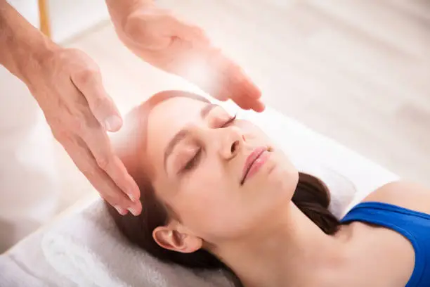 Close-up Of Therapist's Hand Performing Reiki Treatment On Young Woman In Spa