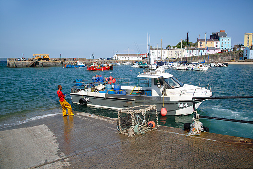 Tenby, UK: June 11, 2018: A fisherman pulls at a rope as he ties a fishing boat to the dock in Tenby Harbour. The welsh name for Tenby can be roughly translated as 'place of the fish' a clear indicator of the importance of the fishing industry to the life of the town.