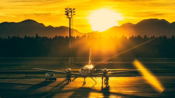 Airplane at an airport landing strip being serviced at sunset. Hills and forests in the background.