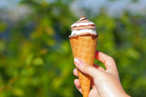 istock Ice cream cone in hand, chocolate ice cream on blurred background, milk dessert on summer vacation, blank for designer, copy space 975239542