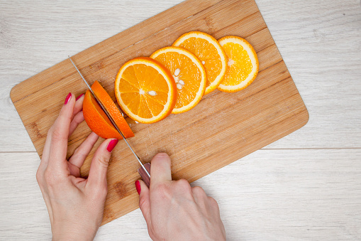 Woman hand slicing orange on wooden board. Housewife or cook in kitchen slicing fresh tropical orange fruits for salad or juicing to freshness. Summer and diet concept