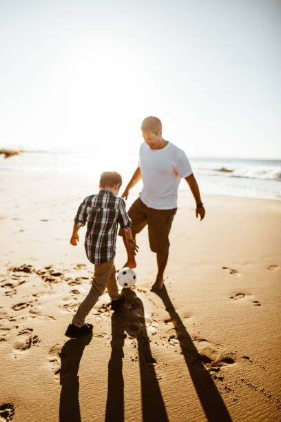 istock dad and son playing together at soccer on the beach 975258012