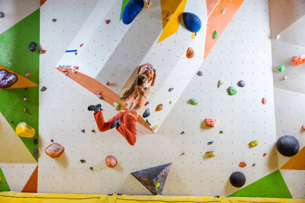 Young athletic woman jumping on climbing hold in bouldering gym stock photo