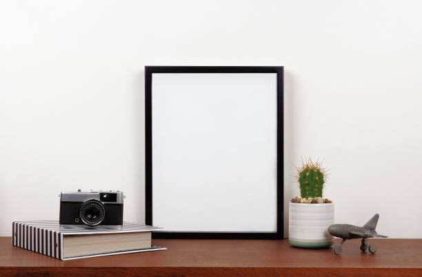 Mock up black frame against white wall with travel decor on a wood shelf