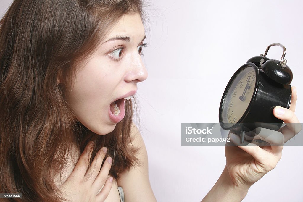A girl holding alarm clock with alarmed expression Portrait of the scared girl holding an alarm clock in a hand. Adult Stock Photo