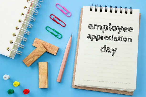 Photo of Text Employee appreciation day on white paper book and office supplies on blue desk / business concept