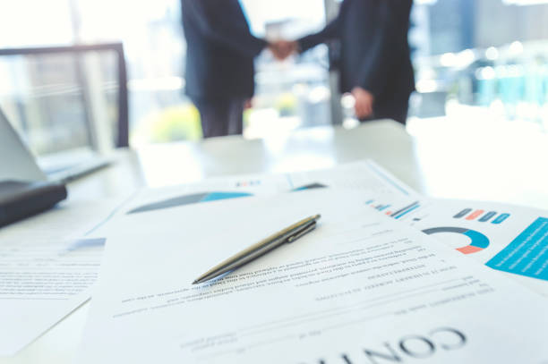 istock Contract on a board room table with men shaking hands. 975415460