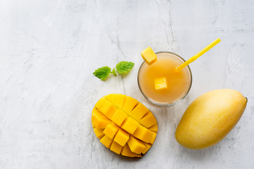 Healthy mango smoothie drink in a glass with mint on concrete table.