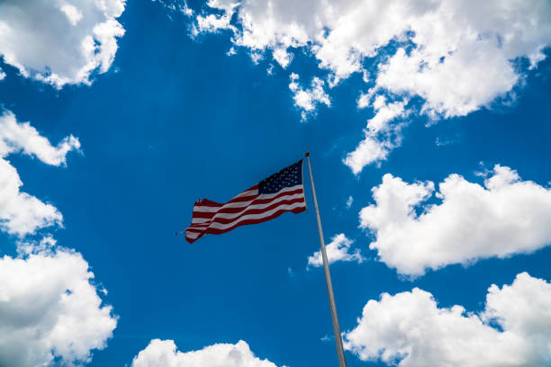 American flag on perfect flag pole clear and sharp  perfect American flag rising up to blue sky with white puffy clouds surrounding flag