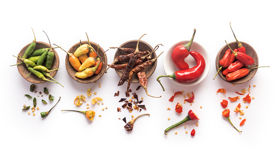 Properly isolated on a pure white background, a series of several cups with a variation of different chili pepper spices. Studio shot and directly above.