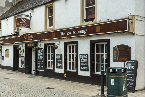 Fort William, Scotland - June 11, 2012: White and brown facade of The Jacobite Lounge bar restaurant in High Street, known also as Ben Nevis Pub. Chalked advertisements. Street scene.