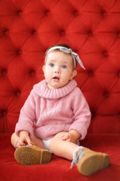 istock Little pretty female child sitting on sofa with red background 975519032