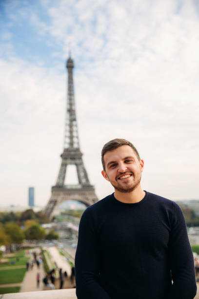 istock Cheerful man in dark blue pullover is standing on the background of the Eiffel Tower 975561404
