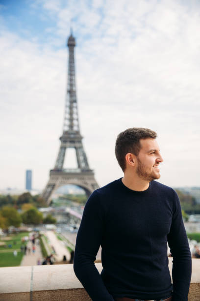 istock Handsome man wearing a dark blue pullover is standing on the background of the Eiffel Tower 975563430