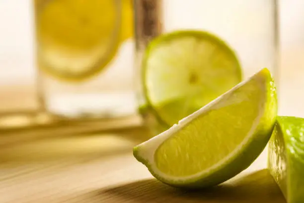 slice of lime on a wooden table with citrus soft drinks in the background, out of focus, one of the glasses is filled with cold water with slices of lemon and the other with slices of lime