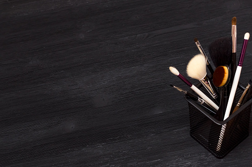 Various make up brushes in metal holder on black wooden table background.