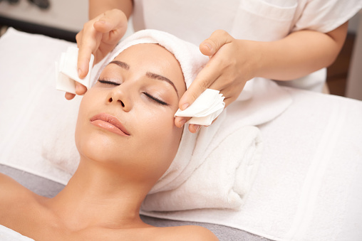 Beautician taking off excess of serum from face of client at the end of spa procedure