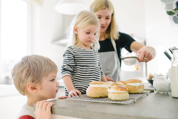 A group of children are making dough on a table. There are several plates of dough on the table, and a few hot dogs are on the table as well