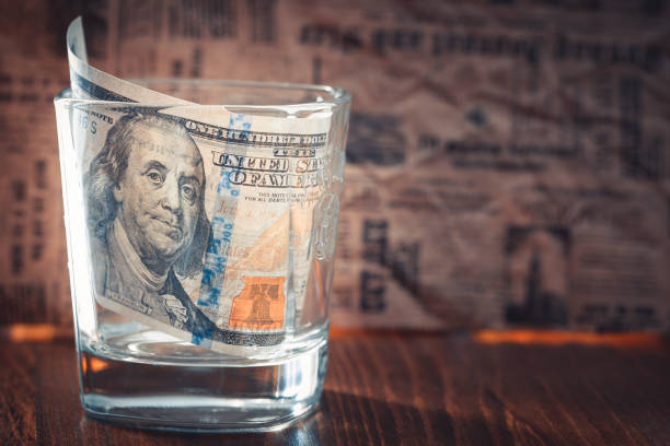 100 dollar bill in whiskey glass on newspaper background
