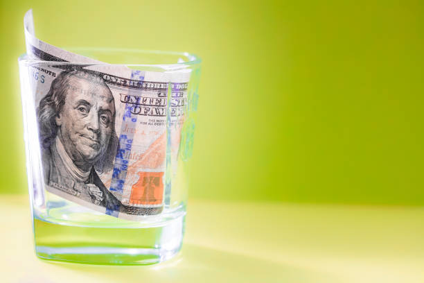 istock 100 dollar bill in whiskey glass on green background 975620492